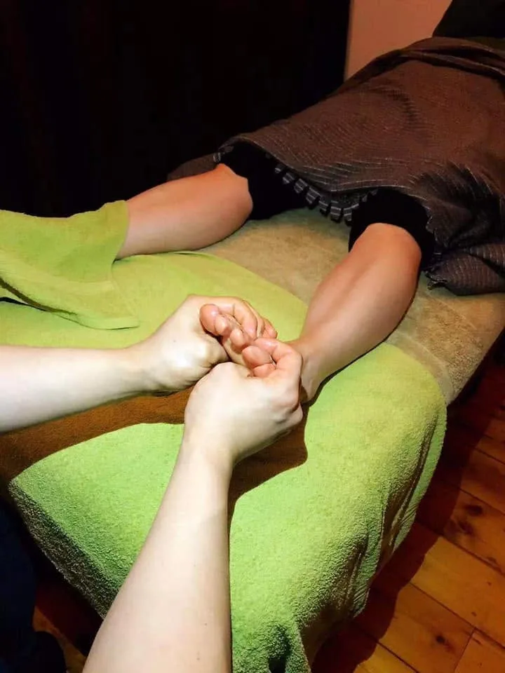 A therapist's hands working the sole and toes of a client's bare foot, lime-green towels